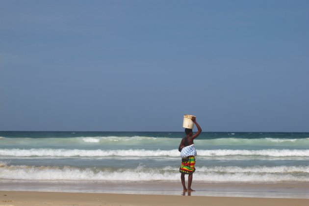 Vrouw met baby op de rug op strand van Dakar