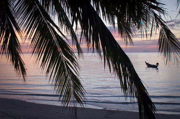 Een bootje dobbert eenzaam vlak na zonsondergang op Koh Pha Ngan