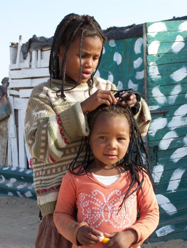 Meisje vlecht haar van ander meisje in township Swakopmund