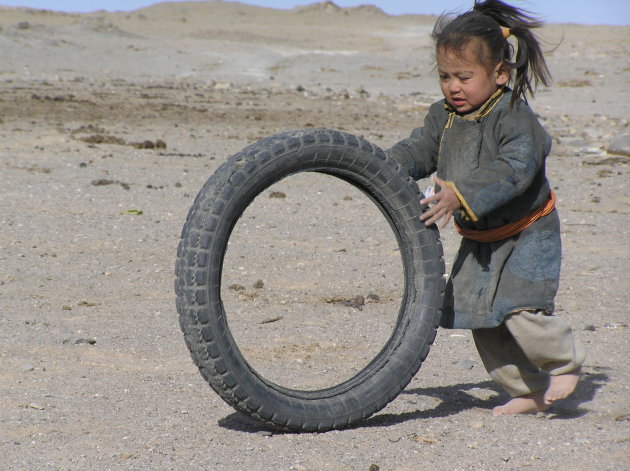 Kindje vermaakt zich in de Gobiwoestijn met een oude buitenband