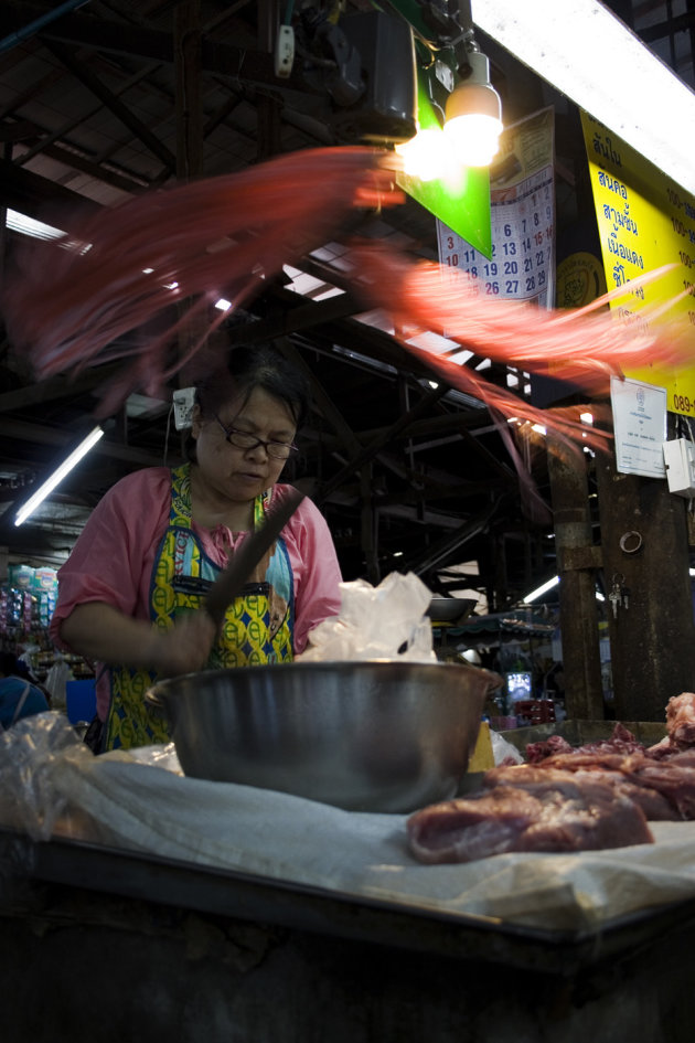 Vrouw bereidt vlees aan zelfgemaakte kraam op lokale markt in Chiang Mai.