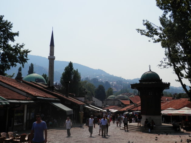 Beeld van een pleintje bij een moskee in Sarajevo, op de achtergrond bergen. 