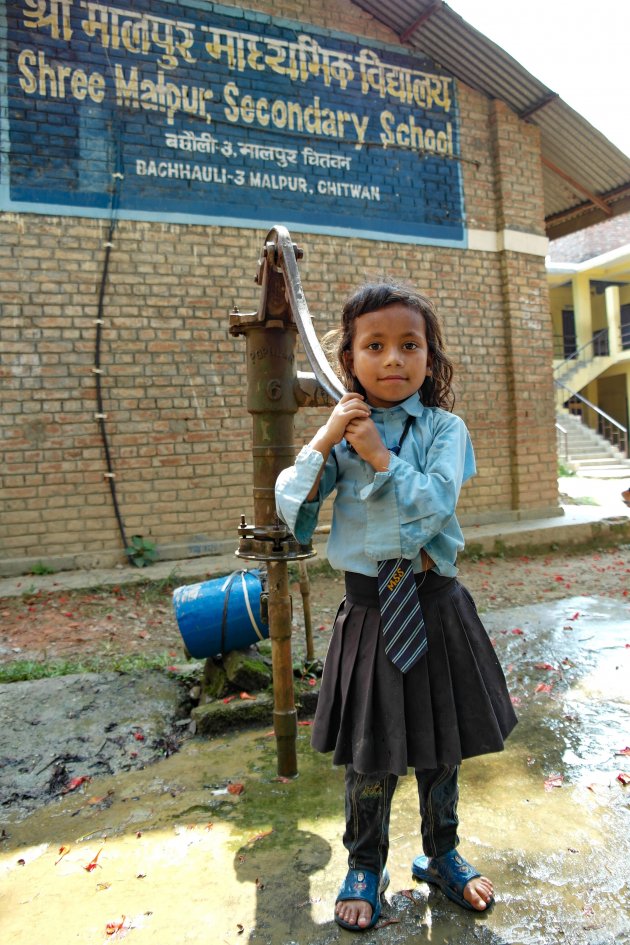 Een leerling pompt het water uit de put op het schoolplein